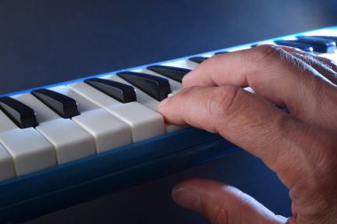 Detail of hand playing blue melodica with blue background and light beam illuminating. clipart