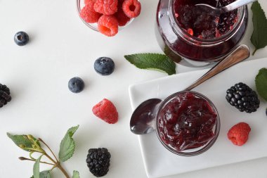 Orman meyvesi reçeli kavanozlar beyaz bir masada ve etrafında yapraklar. Üst görünüm.