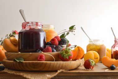 Kırsal ahşap bir masa ve beyaz izole bir zemin üzerinde farklı meyveleri olan çeşitli aromalı birkaç kavanoz reçel. Ön görünüm.