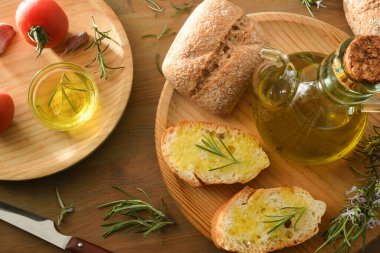 Biberiye esanslı yağla tatlandırılmış ekmek dilimleri ahşap bir masada biberiye filizleri ve domateslerle birlikte. Üst görünüm.