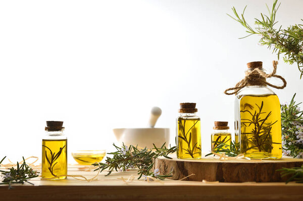 Деталь розмаринового масла в стеклянной бутылке, приготовленной дома с веточками на деревянном столе и керамическим раствором и пестиком и белым изолированным фоном. Вид спереди.