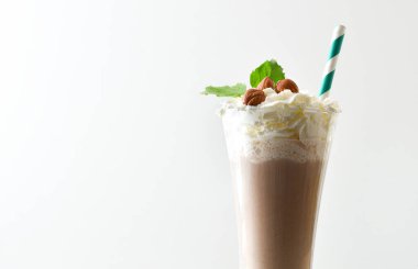 Fındıklı milkshake ve fındıkla süslenmiş krema ve saman ve beyaz arka planlı yapraklı bir bardak. Ön görünüm.