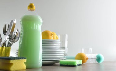 Çevre dostu bulaşık makinesi, bulaşık yıkamak için bir şişe dolusu ürün, temizleme pedleri ve ahşap mutfak tezgahında limonlu tabaklar ve izole edilmiş beyaz arka plan. Ön görünüm.