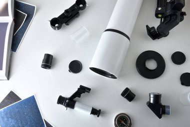 Parçalanmış bir teleskopun parçaları, içinde resimler ve kitap olan beyaz bir masanın üzerinde. Üst görünüm.