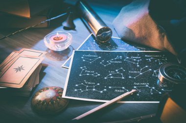 Takımyıldızlı haritalı esrarengiz astrolojik arka plan detayları, kehanet kartları ve sihirli atmosferli ahşap masa üzerindeki eski nesneler. Yüksek görünüm.