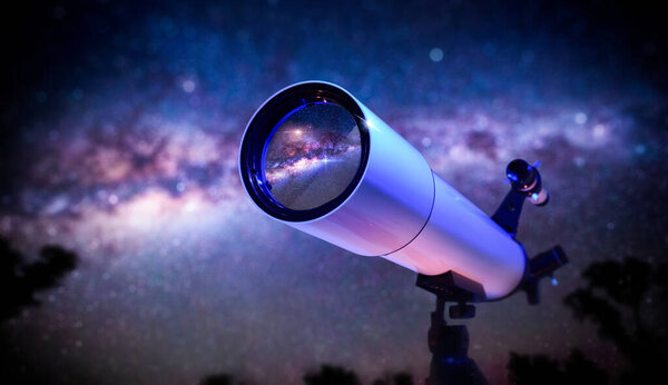 Detail of font of white telescope on tripod pointing at a starry sky at dusk.