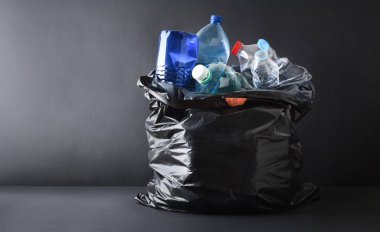 Siyah plastik çöp torbalarıyla dolu arka planda karanlık arka plan ve üste izole edilmiş plastik kaplar. Ön görünüm.