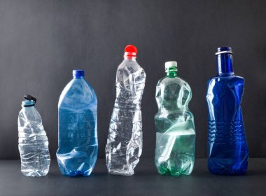 Plastik kirliliği ve geri dönüşüm konsepti. Siyah arka planda izole edilmiş siyah bir üste sıralanmış plastik şişeler. Ön görünüm.