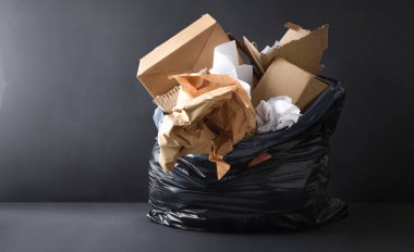 Siyah plastik çöp torbasının detaylarıyla arka plan. Koyu arka plan ve tabanda izole edilmiş kağıt ve karton dolu. Ön görünüm.