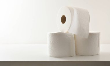 Üç yumuşak istiflenmiş tuvalet kağıdı rulosu beyaz ahşap masa ve beyaz yalıtılmış arka plan. Ön görünüm.