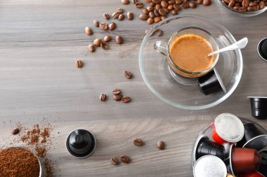 Kahve bardağı ve kahve tozu için kapsüllü kapsülleri olan ahşap bir bankta cam bir fincanda Espresso kahvesi. Üst görünüm.