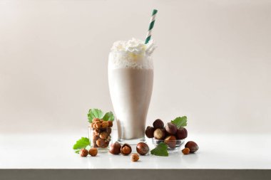 Kremalı fındıklı smoothie ve yeşil pipetli fındık dolu kaseler ve izole ışık arka planında yapraklar. Ön görünüm.