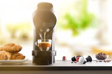 Mutfak tezgahında kahve makinesiyle kahvaltı kahvesi hazırlamak. Kapsüller, kahve çekirdekleri ve parlak bir mutfakta hamur işleri. Ön görünüm.