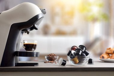 Kapsüllü, fasulyeli ve pastalı ahşap bir bankta espresso makinesinde taze demlenmiş kahve, arka planda oturma odası var. Yan görünüm.