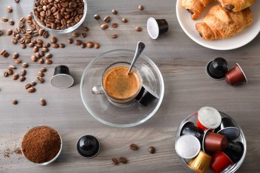 Bardakta bir fincan espresso ve kahve çekirdekleri, kahve fincanları, kapsüller ve hamur işleriyle dolu bir tabağın üzerinde bir fincan kahve ile kahvaltı. Üst görünüm.