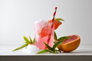 Meyve, buz ve beyaz izole arkaplan yaprakları ile beyaz bir masa üzerinde bir dilim meyve ve bir kamış ile dekore edilmiş cam bir fincanda buzlu greyfurt içeceği tazeleniyor. Ön görünüm.