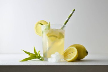 Kamışla süslenmiş cam bardakta buzla limon içeceği ve beyaz bir masada meyve, buz ve beyaz izole arkaplanlı yapraklarla meyve dilimi. Ön görünüm.