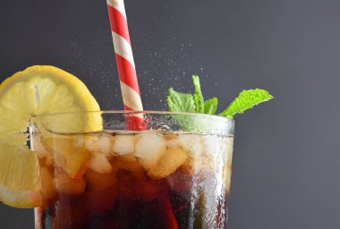 Nane ve limonla süslenmiş ferahlatıcı buzlu cam bardak ve gri izole arkaplanlı kırmızı ve beyaz kamış. Ön görünüm.