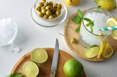 Nane, limon ve limona dayalı ferahlatıcı bir içecekle mutfak tezgahı. Kesme tahtası, meyve, buz ve zeytinli kaplar. Üst görünüm.