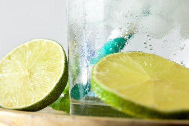 Bir bardağın tabanının ayrıntıları, etrafında bir kamış, buz ve limon dilimleri ve nane ile ferahlatıcı bir içecek. Ön görünüm.