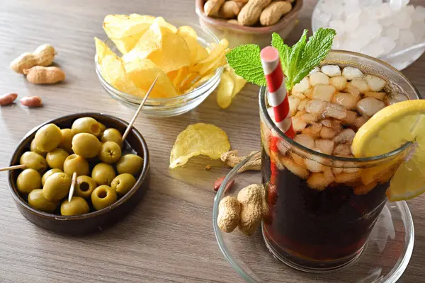 Zeytin, patates ve fıstık ile dolu ahşap bir masada kola ve atıştırmalık kaplar. Yüksek görünüm.