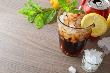 Buzla, nane yapraklarıyla, limonlarla ve bir kutu kolayla dekore edilmiş ahşap bir masanın üzerindeki bardakta naneli ve limonlu kola kokteyli. Yüksek görünüm.