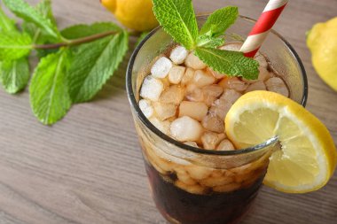 Buzla, nane yapraklarıyla, limonlarla ve bir kutu kolayla dekore edilmiş ahşap bir masanın üzerindeki bardakta naneli ve limonlu kola kokteyli. Üst Görünüm.