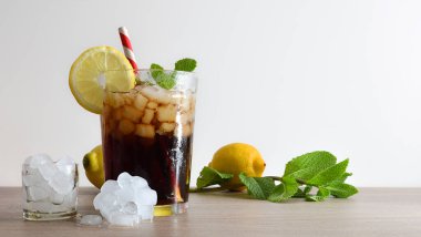 Cam bardakta buzla canlandırılmış kola içeceği. Pipetle süslenmiş ve ahşap bir masada meyve dilimi. Meyve, buz ve nane yaprakları ve beyaz izole bir arka plan. Ön görünüm.