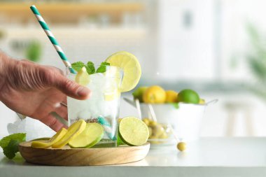 Limonlu, limonlu soda içen ve limonlu, limonlu, mutfak arkaplanlı beyaz mutfak tezgahında bolca buz içen kişi. Ön görünüm.