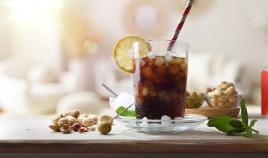 Odasında nane yaprağı ve limon dilimleri ile süslenmiş fıstık ve zeytin gibi abur cuburlarla ahşap bir masada kola içmek. Ön görünüm.
