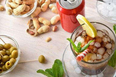 Nane yaprağı ve limon dilimleriyle süslenmiş fıstık ve zeytin gibi abur cuburlarla ahşap bir masada kola içmek. Üst görünüm.