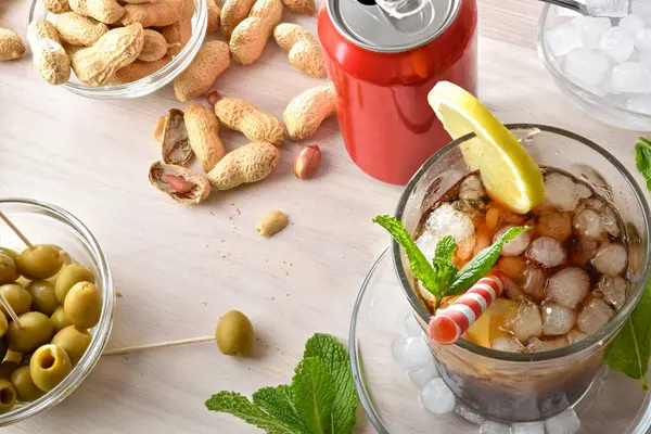 Nane yaprağı ve limon dilimleriyle süslenmiş fıstık ve zeytin gibi abur cuburlarla ahşap bir masada kola içmek. Üst görünüm.