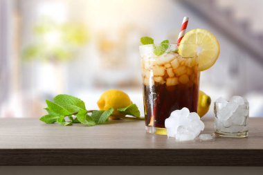 Oturma odasında meyve, buz ve nane yapraklarıyla bezenmiş bir masa üzerinde pipetle süslenmiş cam bir bardaktaki buzla kola içeceğini tazeliyorum. Ön görünüm.