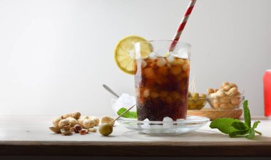 Fıstık ve nane yapraklarıyla süslenmiş zeytinler ve beyaz izole edilmiş arkaplanlı limon dilimi gibi atıştırmalıklarla ahşap bir masada karbonatlı kola içeceği tazeliyorum. Ön görünüm.