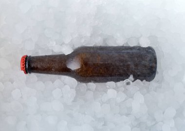 Arka planda içi bira dolu kahverengi bir şişe var, yarısı buz küplerinin içinde gömülü. Üst görünüm.