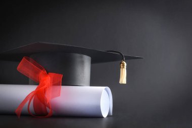 Siyah arka planda kırmızı kurdeleli akademik başlık ve diploma. Ön görünüm.