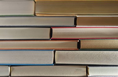 Ahşap bir raftaki ön kenarı ve karanlık izole edilmiş arkaplanı gösteren bir yığın kitabın ayrıntıları. Ön görünüm.