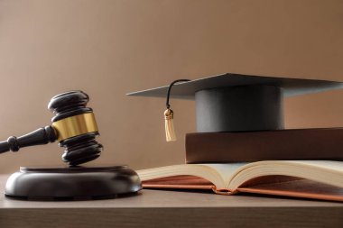 Eğitim konularında yargıcın tokmağının ahşap masada, havan tahtasının üstünde kitap yığını ve kahverengi izole arka planda olduğu yargı kavramı. Ön görünüm.