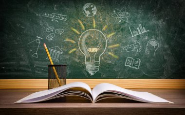 Eğitim alanında öğrenim ve bilgi kavramı, tahtadan bir masa üzerinde açık bir kitap ve farklı eğitim konularını ve ampulü temsil eden çizimlerle dolu bir karatahta..
