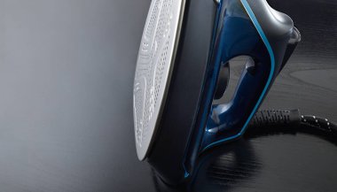 Siyah ve mavi buharlı ütünün ayrıntıları siyah ahşap bir masanın üzerinde dikey olarak duruyor, metal tabanı buhar delikleriyle gösteriyor..