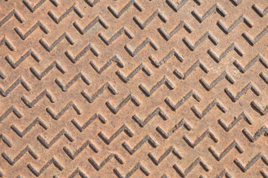 Üzerinde zikzak deseni olan paslı metal bir rögar kapağının makro detayları. Üst görünüm.