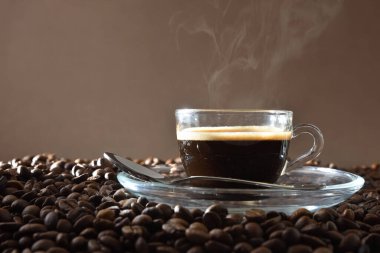 Kahverengi izole edilmiş kahve çekirdeği yığınının üzerinde tadımlık olarak sıcak kahve ile el ele tutuşan kahve fincanı. Ön görünüm.