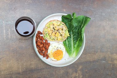 bread with egg and avocado topping with sunny side up egg , lettuce , almond and americano coffee for serve clipart