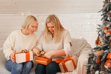 Mutlu kadın anneler Noel için hazırlanıyor, yeni yıl hediyeleri evde Noel ağacının yanında otururken paketleniyor. Kış tatili, ev dekorasyonu konsepti