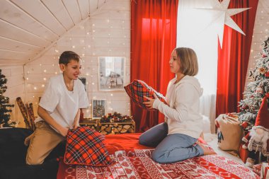 Çocuklar Noel süslemeli yatak odasındaki yastıklarla, yastık savaşıyla, yeni yıl tatili konseptiyle oynarlar.