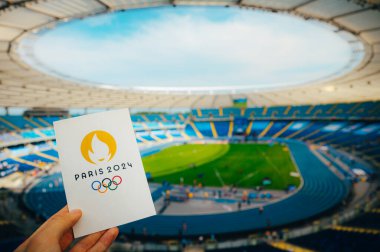 PARIS, FRANCE, JULY 7, 2023: Icon of Summer olympic Games Paris 2024 Held by Athlete. Modern Olympic Stadium in background. Wallpaper for Summer Olympic Game in Paris 2024. clipart