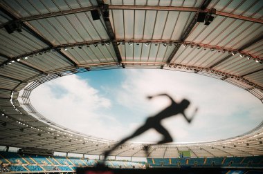 Bir Atletin Silüeti, Özgüvenli ve Odaklanmış, Modern Spor Stadyumunda Alacakaranlık Parıltısını Kucaklayan.