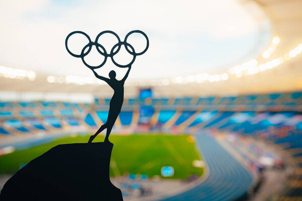 PARIS, FRANCE, JULY 7, 2023: Statue of athletics Woman holding above head olympic circle. Modern Olympic Stadium in Background. Sport photo for Summer olympic Game in Paris 2024