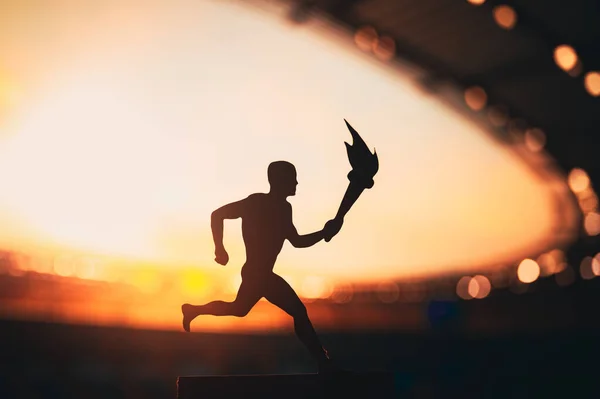 Silhouette of Male Athlete Carrying the Torch Relay, Illuminating the Modern Track and Field Stadium. A Captivating Snapshot for the Summer Game 2024 in Paris.