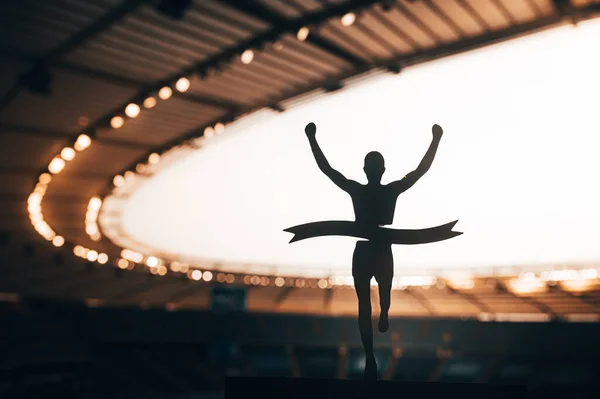 Conquering the Finish Line: Silhouetted Runner\'s Victory Stirs the Atmosphere at Modern Athletics Stadium. A Compelling Image of Track and Field Triumph. Warm color Tone photo for Summer in Paris 2024